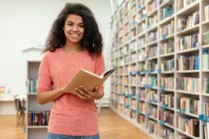 girl holding book in front of large bookcase